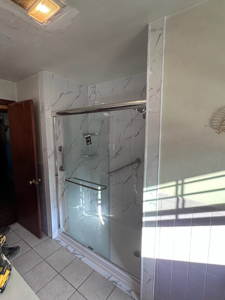 Walk-in shower with marble-look acrylic walls and a sliding glass door
