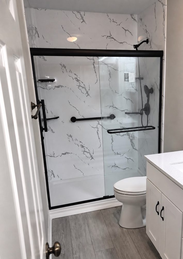 Remodeled bathroom with a marble-look walk-in shower, black-framed glass door, new vanity and flooring