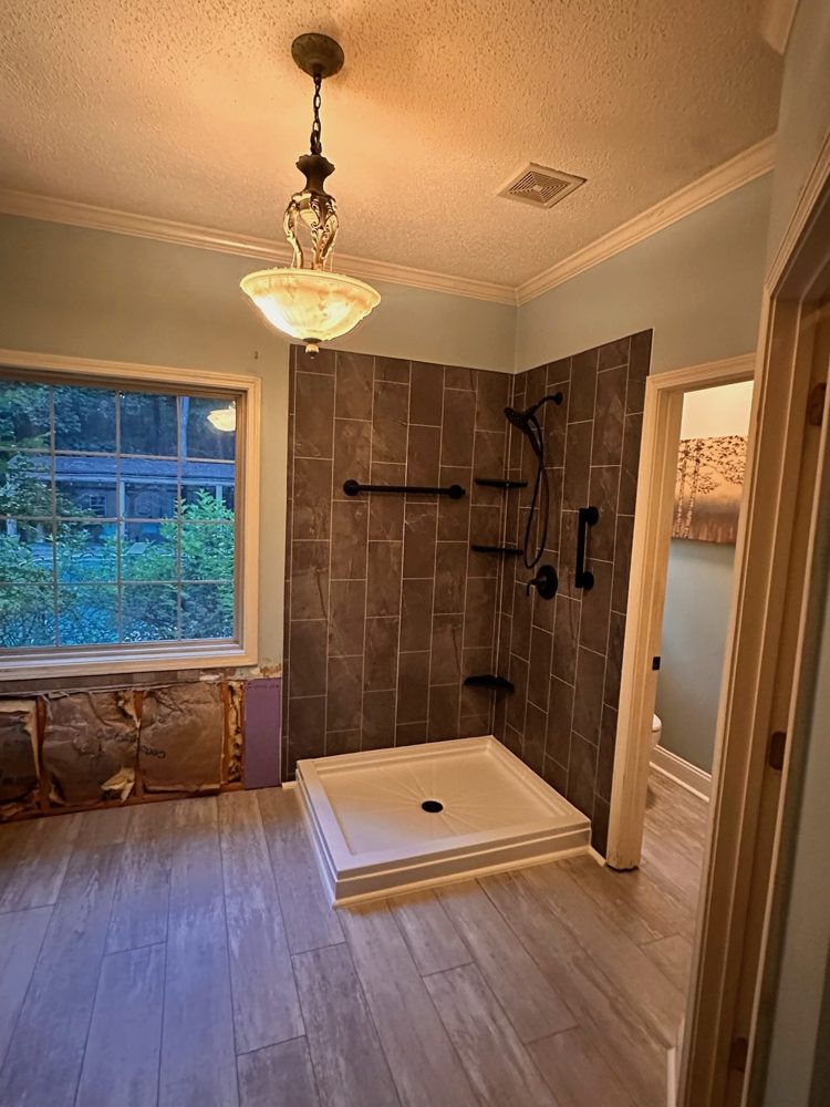 Custom walk-in shower with brown tile-look walls, black grab bars and a custom base