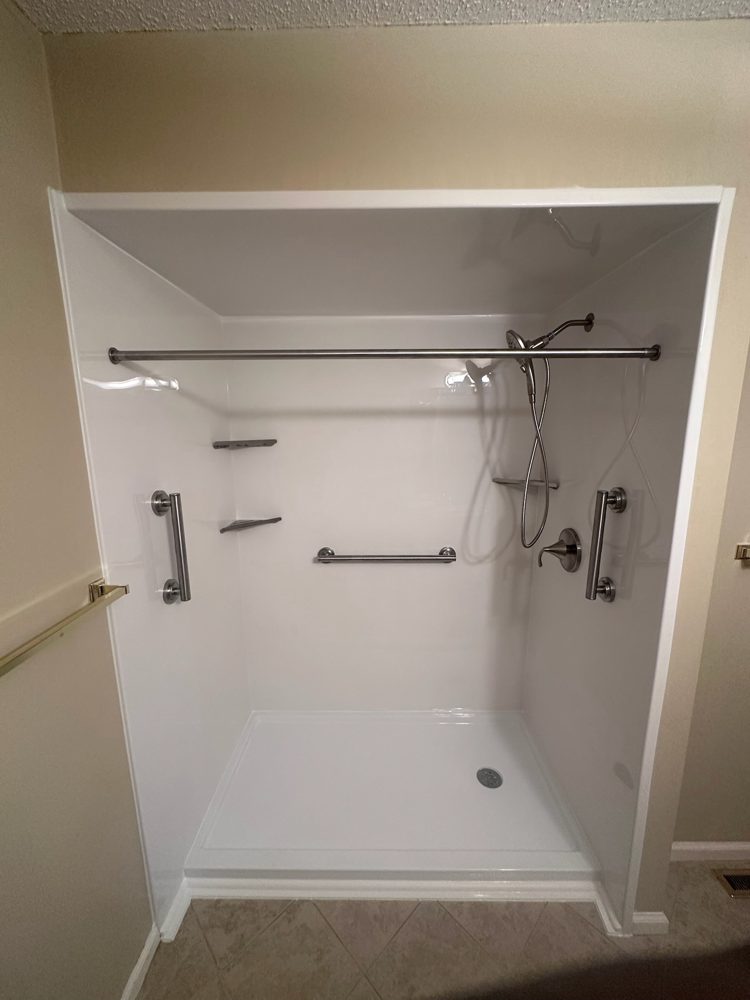 Simple walk-in shower with white acrylic walls, grab bars and a low step-in base, no door