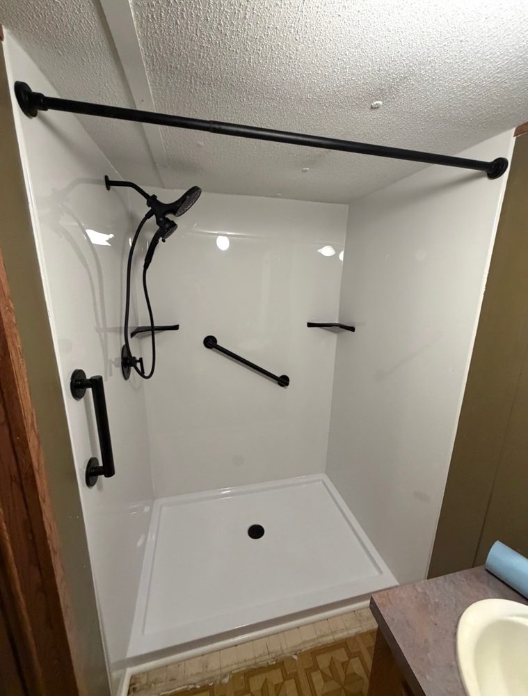 Walk-in shower with white acrylic walls, black fixtures and grab bars installed by Carolina Bath Solutions