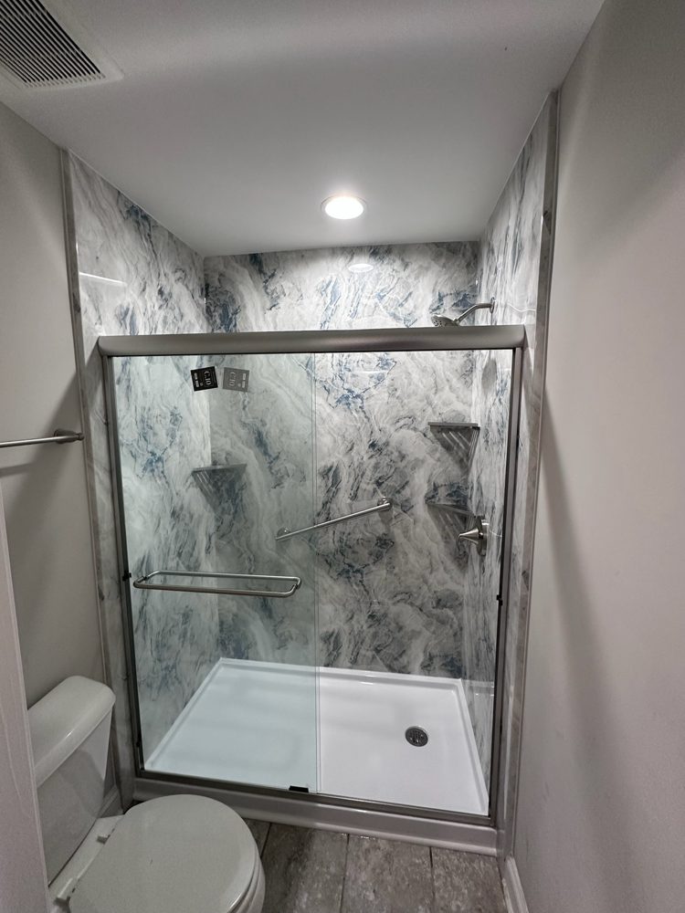 Walk-in shower with blue and white marble-look acrylic walls and a framed glass door