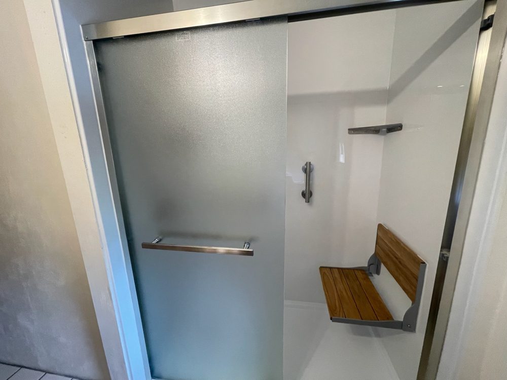 Walk-in shower with a frosted glass door and a fold-down teak seat in a Charlotte-area home