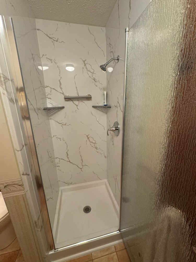 Walk-in shower with marble-look acrylic walls and a frosted glass door