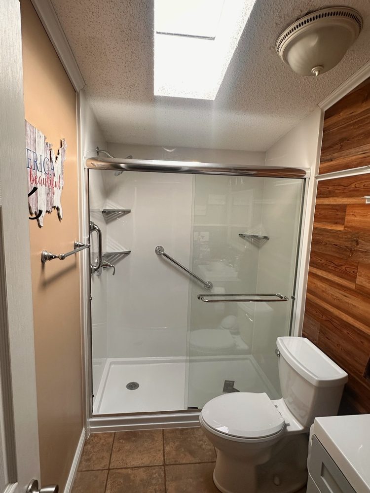 Walk-in shower with grab bar and glass door in a bright bathroom with a skylight