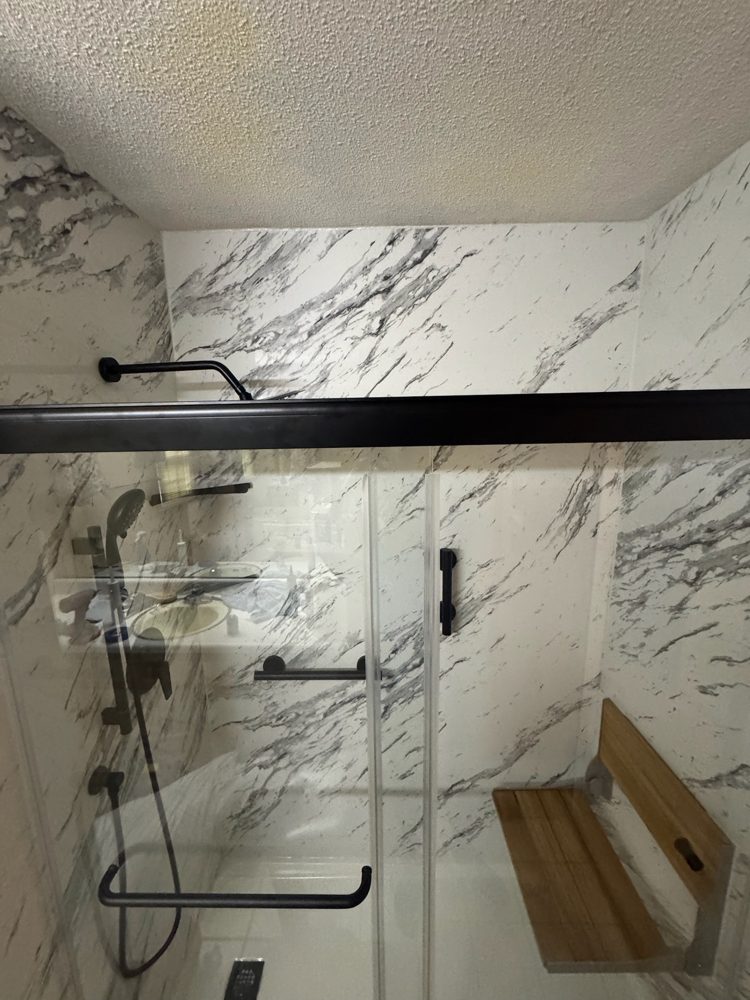 Walk-in shower with marble-look walls, black fixtures and a fold-down teak seat