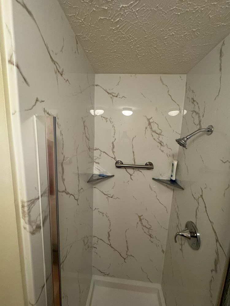 Finished walk-in shower with marble-look acrylic walls and a glass door